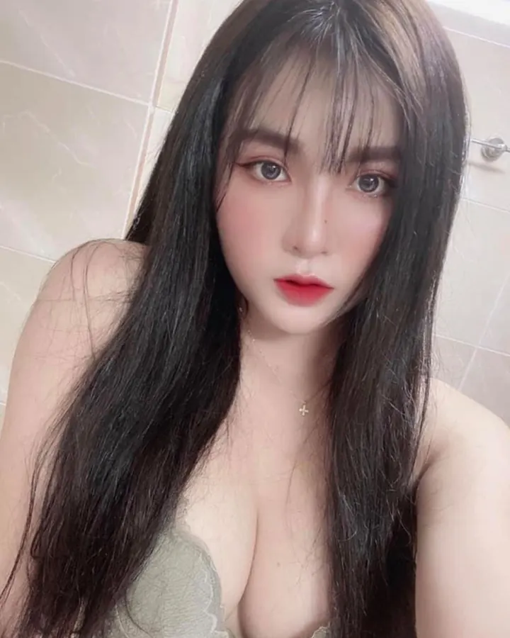Jeune femme asiatique aux cheveux châtains, yeux bleus, vêtue d'un haut vert, posant de face dans une salle de bain, le regard fixe.