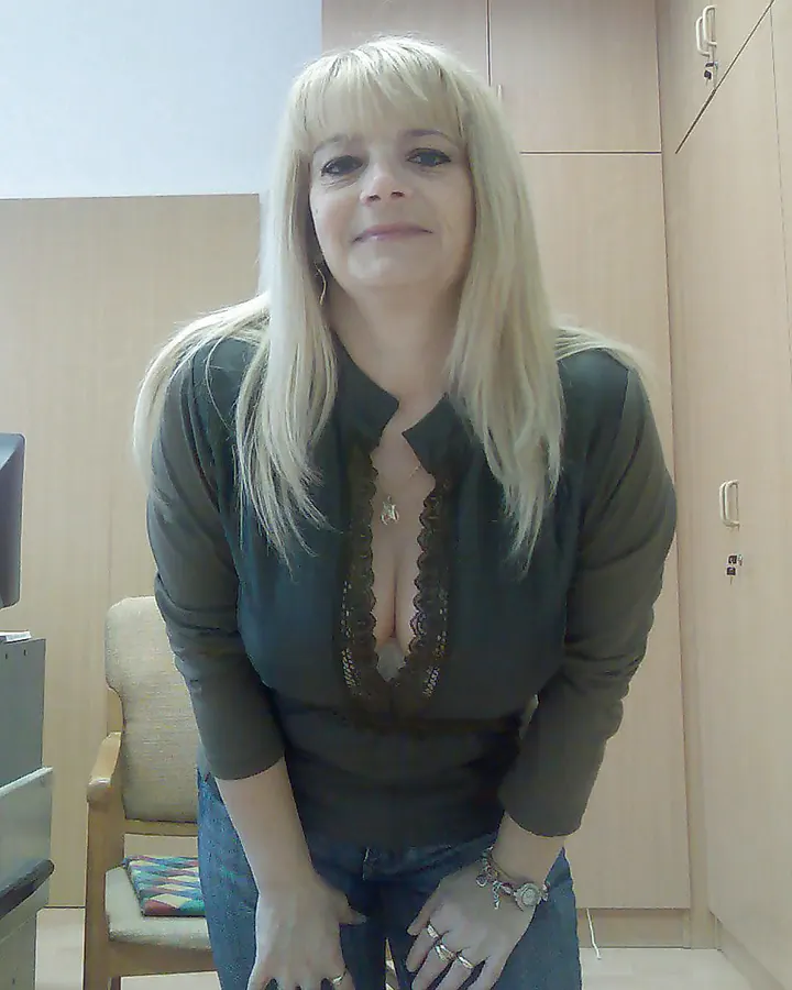 Femme blonde en lingerie noire, assise sur un lit, les jambes croisées, regardant l'appareil avec un air sensuel.