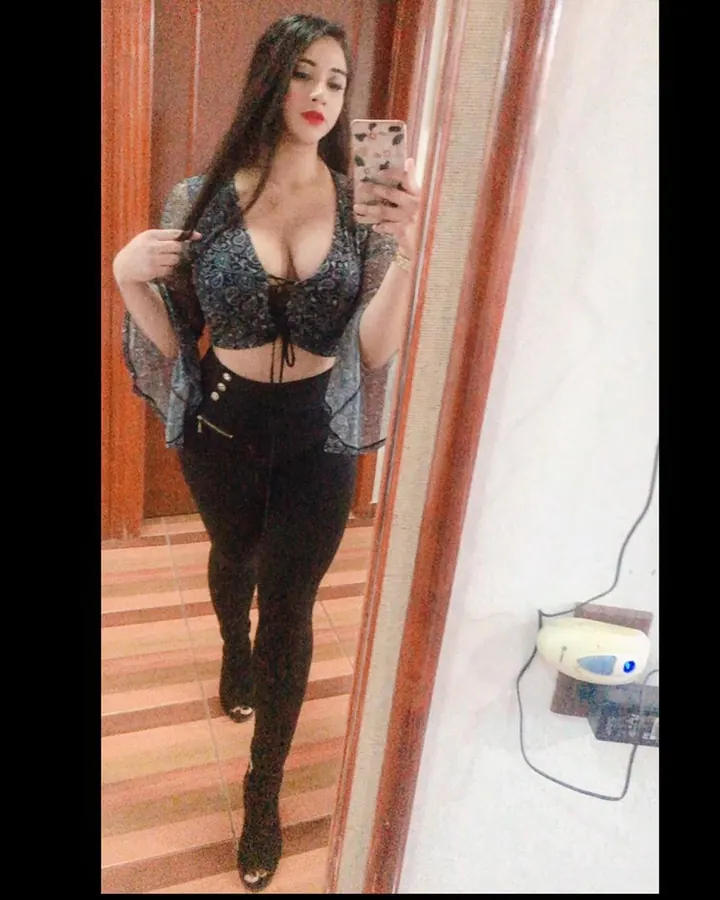 Jeune femme aux cheveux bruns, portant un haut noir, assise sur un lit, tenant un téléphone.