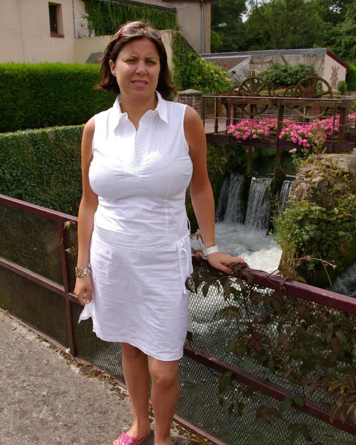 Femme en robe blanche sans manches, debout près d'une rivière, avec des fleurs roses en arrière-plan