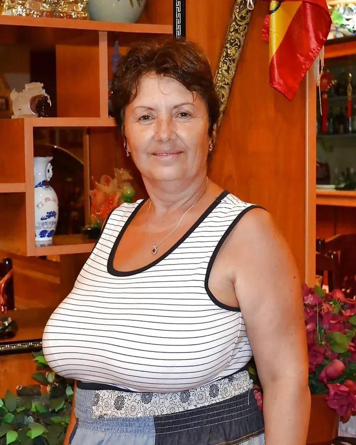Femme aux cheveux bruns en haut blanc, posant en extérieur.