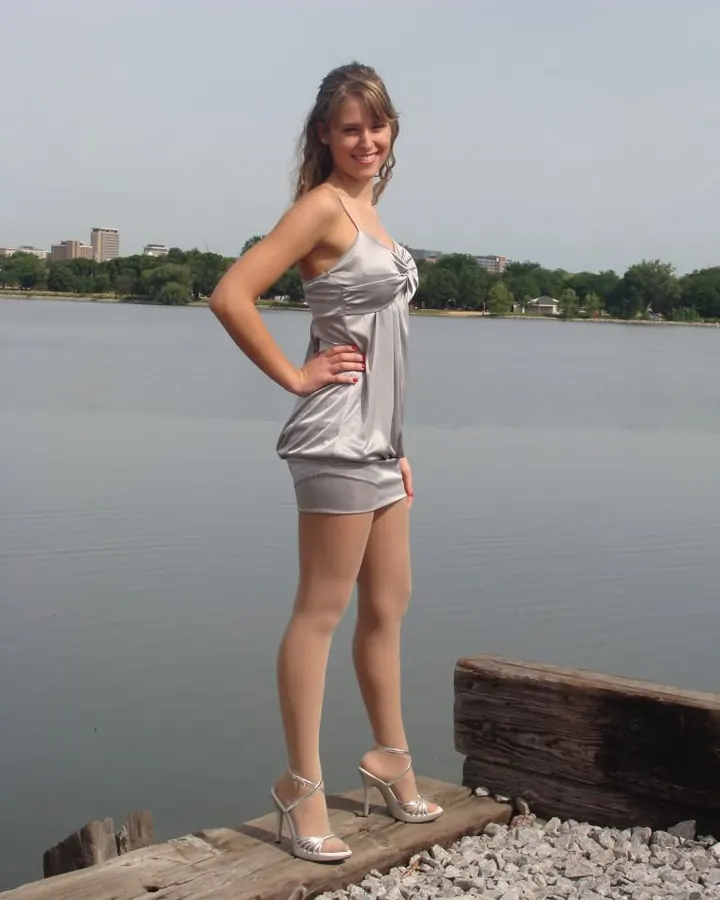 Jeune femme aux cheveux longs portant un haut blanc et un short rayé, assise dans un restaurant avec vue sur la ville la nuit.