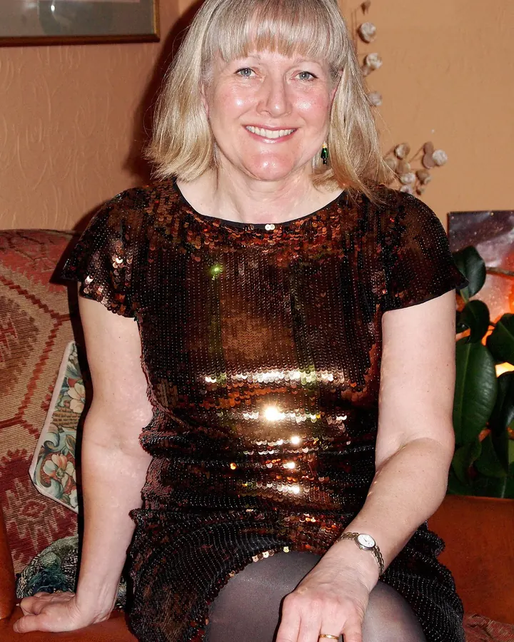 Femme blonde en robe blanche fendue, mains sur les hanches, posant dans un salon