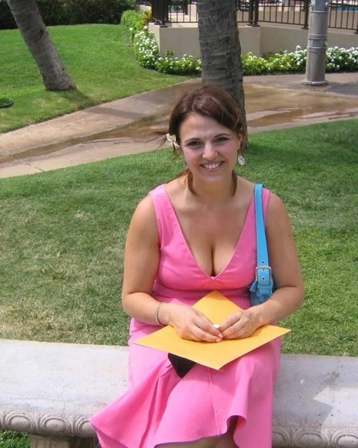 Femme en robe rose, assise sur un banc en pierre dans un parc, tenant une enveloppe jaune.