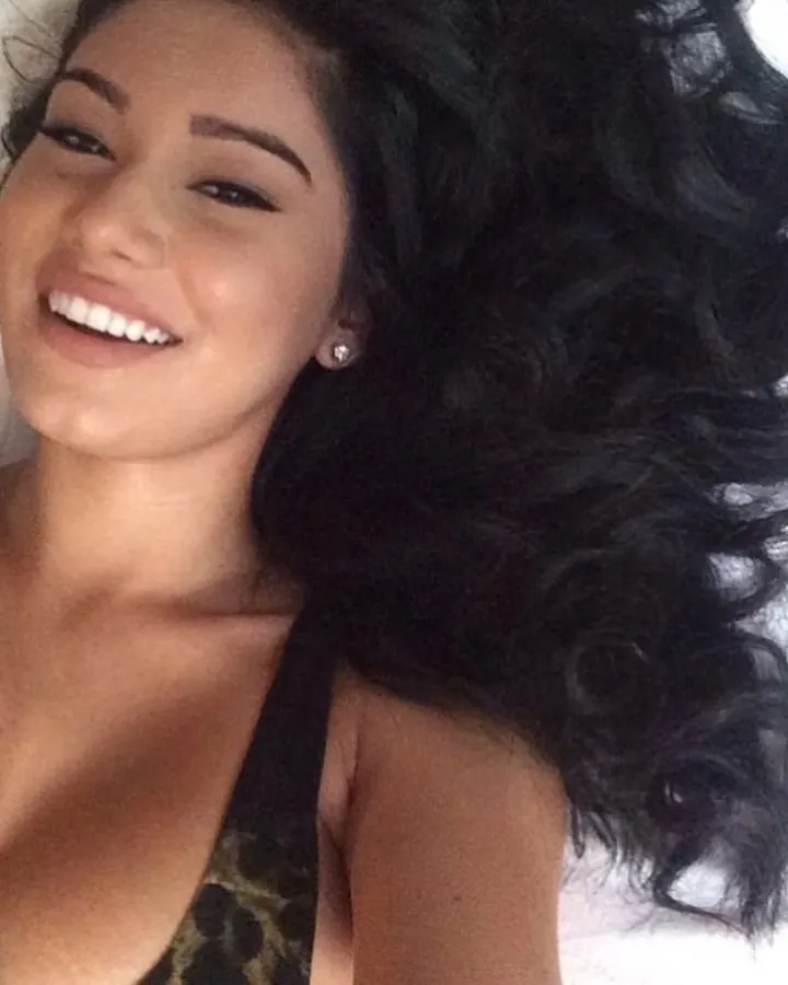 Femme souriante allongée, vêtue d'un haut noir, cheveux noirs ondulés, regardant l'appareil.