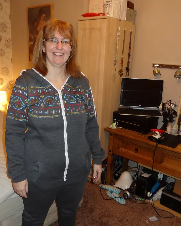 Femme aux cheveux blonds en pyjama gris, debout dans une chambre