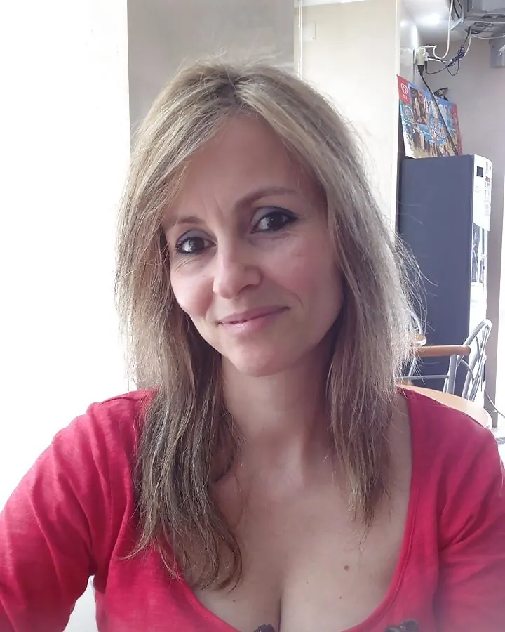 Femme aux yeux marrons et cheveux platine, en chemisier rouge, souriant légèrement à l'appareil.