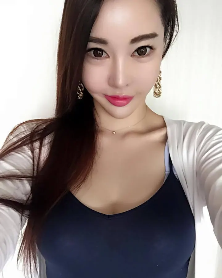 Femme asiatique aux cheveux châtains, regardant directement l'appareil, vêtue d'un haut bleu foncé et d'une veste blanche légère