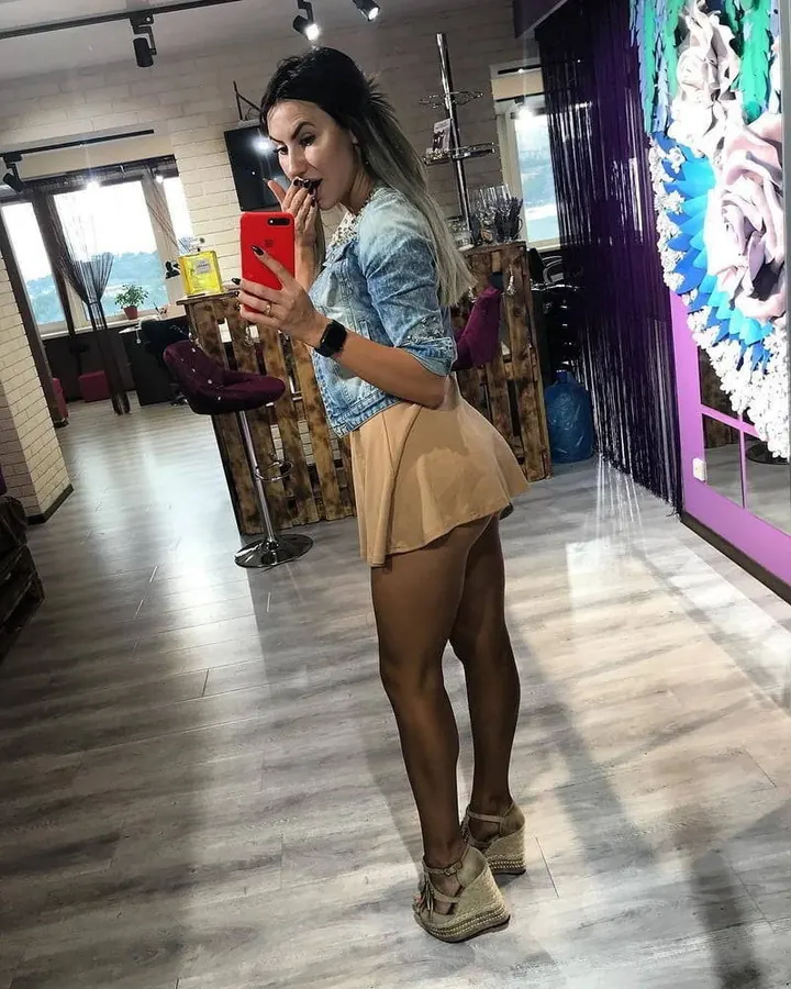 Femme aux cheveux bruns-noirs, en haut noir, prenant un selfie dans une cuisine.