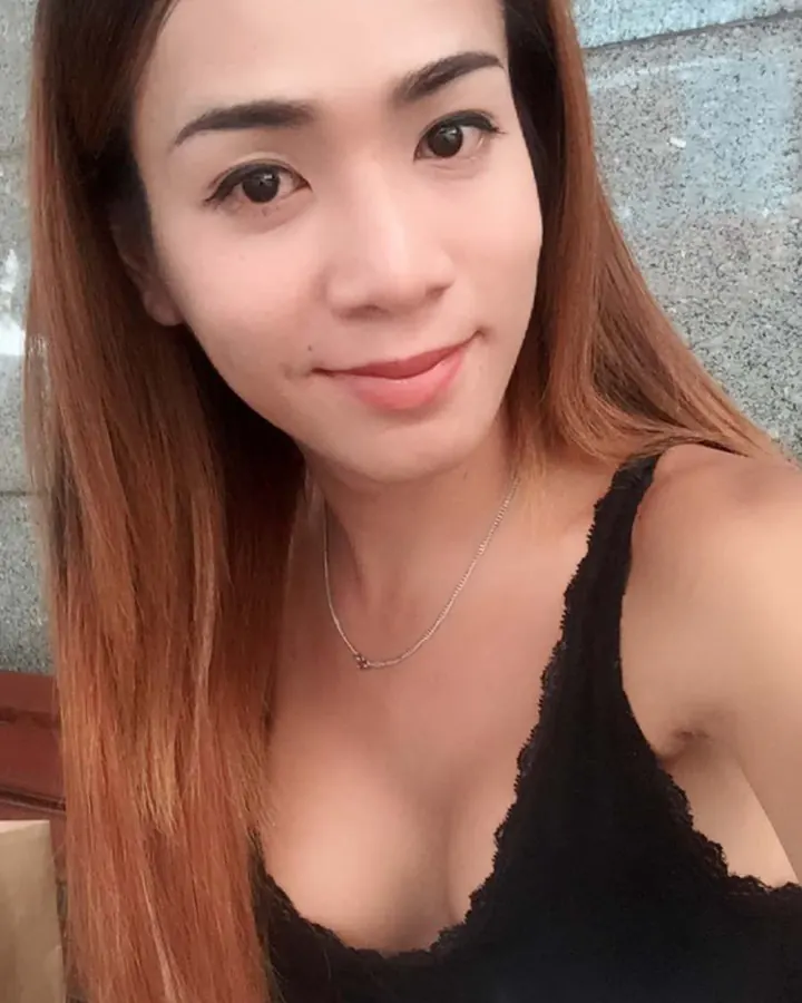 Jeune femme asiatique aux cheveux châtains, souriante, portant un haut noir dentelle et un bas blanc, en extérieur.